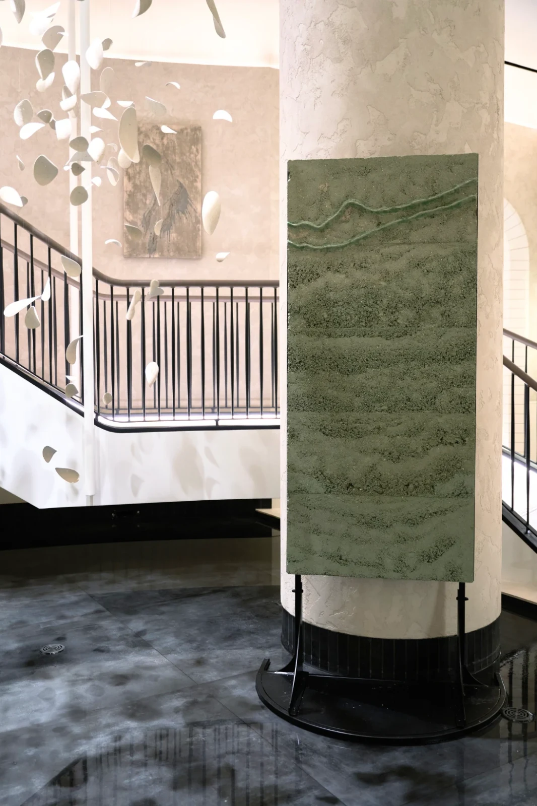 Terre Verte by Adam Weismann, a tall green rammed-earth panel with layered strata and two glassy ridges, on a black stand against a plaster column
