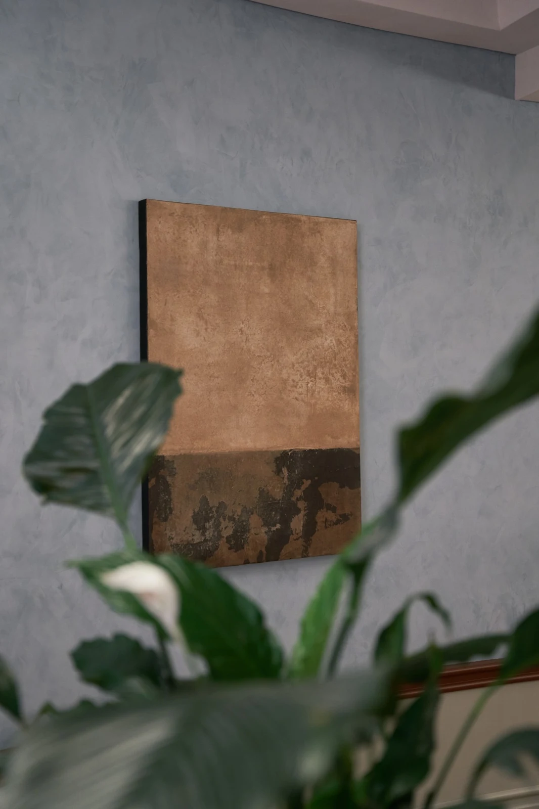 Untitled (GES#2) by Alexandra Yan Wong, on a blue plaster wall seen through leaves