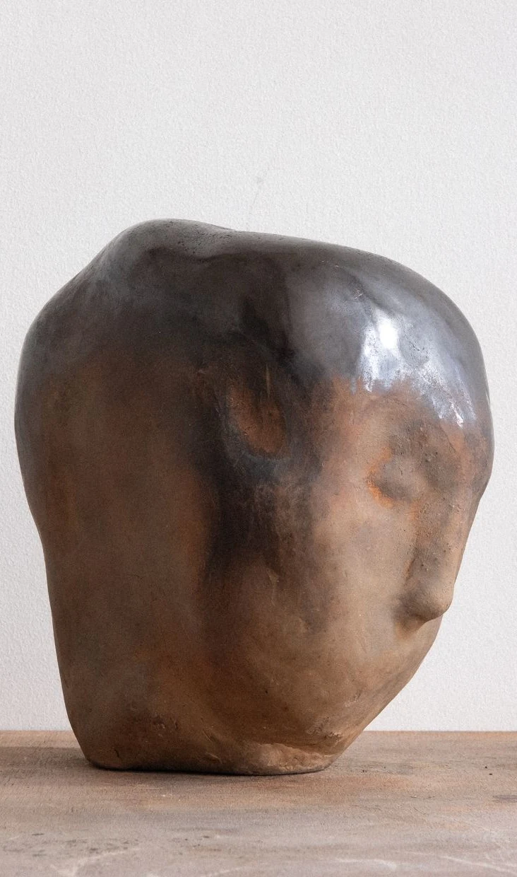 Inbetween Worlds by Arran Gregory, a large burnished clay head with a smoky black crown and warm brown face, turned to the right