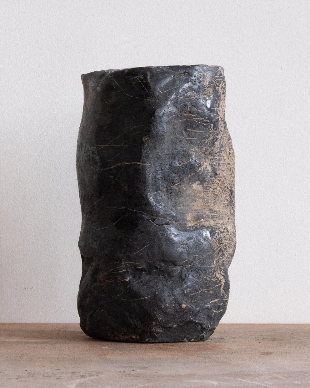 Wheel of Matter by Arran Gregory, a tall dark burnished clay vessel with a crumpled, scratched surface on a wooden table
