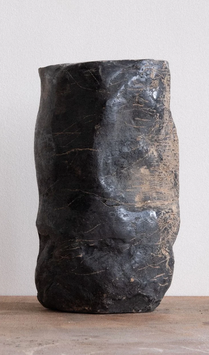 Wheel of Matter by Arran Gregory, a tall dark burnished clay vessel with a crumpled, scratched surface on a wooden table