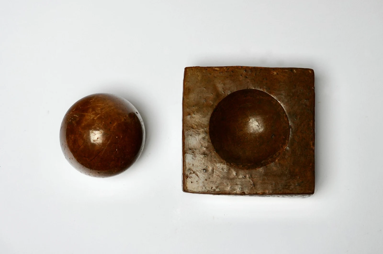 Dorodango Pair II by Edie Evans, a polished clay sphere beside a square block with a round hollow, seen from above