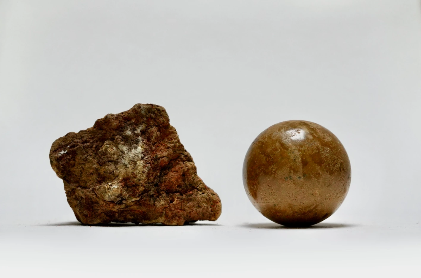 A rough rock beside a burnished clay sphere in Earth Memory by Edie Evans