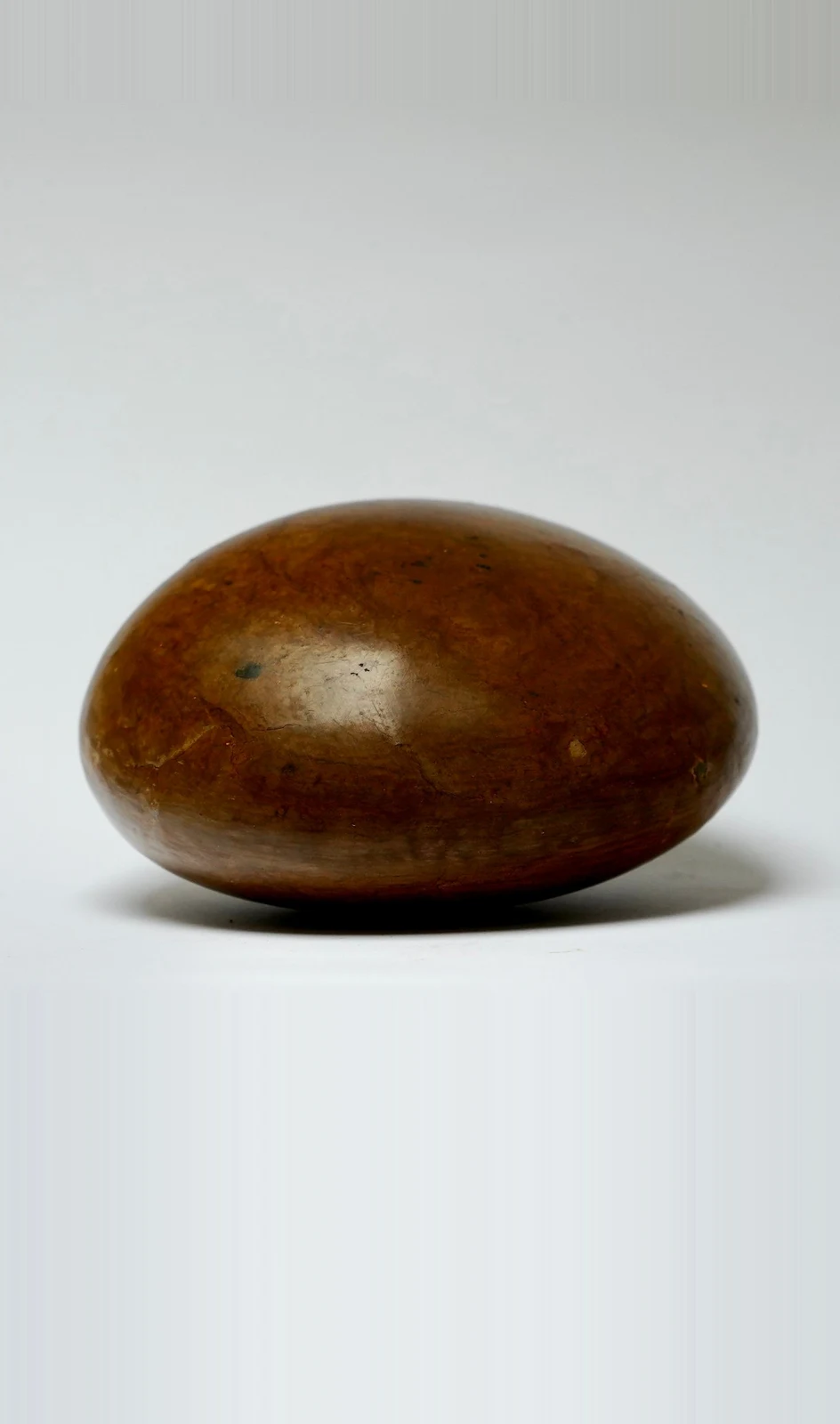 Holding by Edie Evans, a smooth polished clay ovoid resting low on a white surface