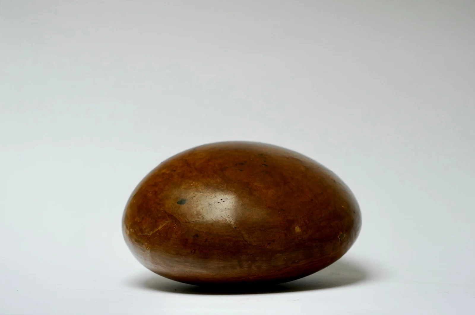 Holding by Edie Evans, a smooth polished clay ovoid resting low on a white surface