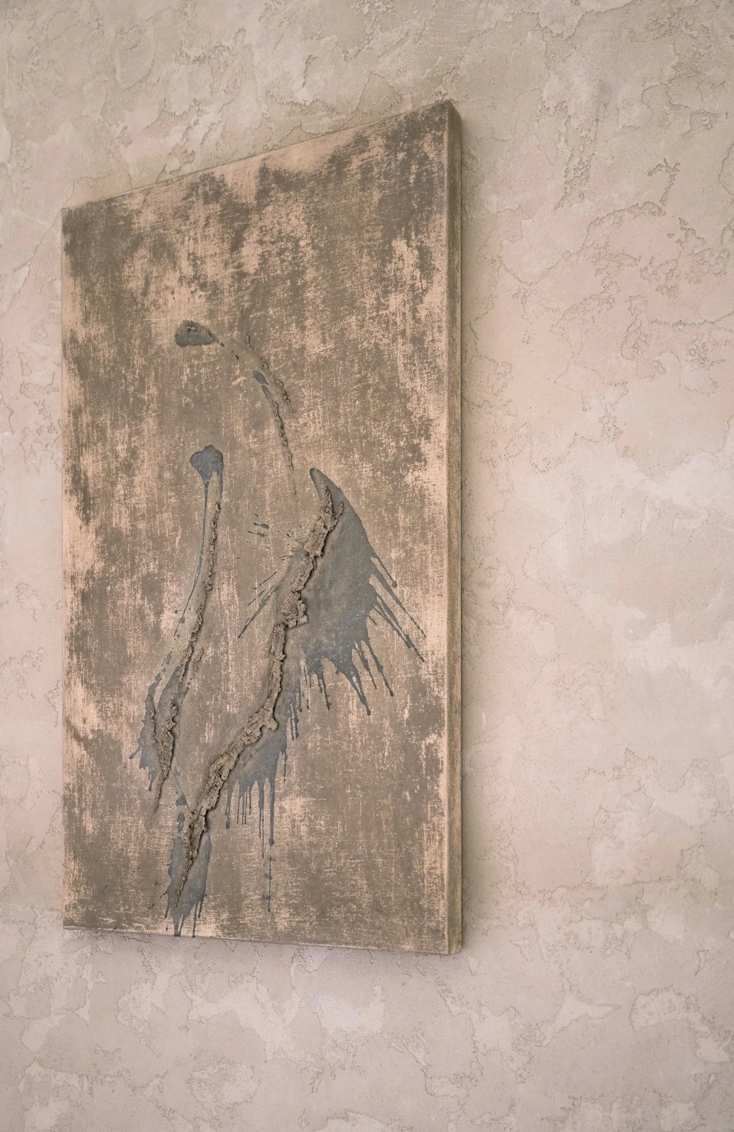 Unearthing Series #1 by Eleanor Herbosch, a tall canvas of pale earth tones with raised grey clay marks and drips, hung on a plaster wall