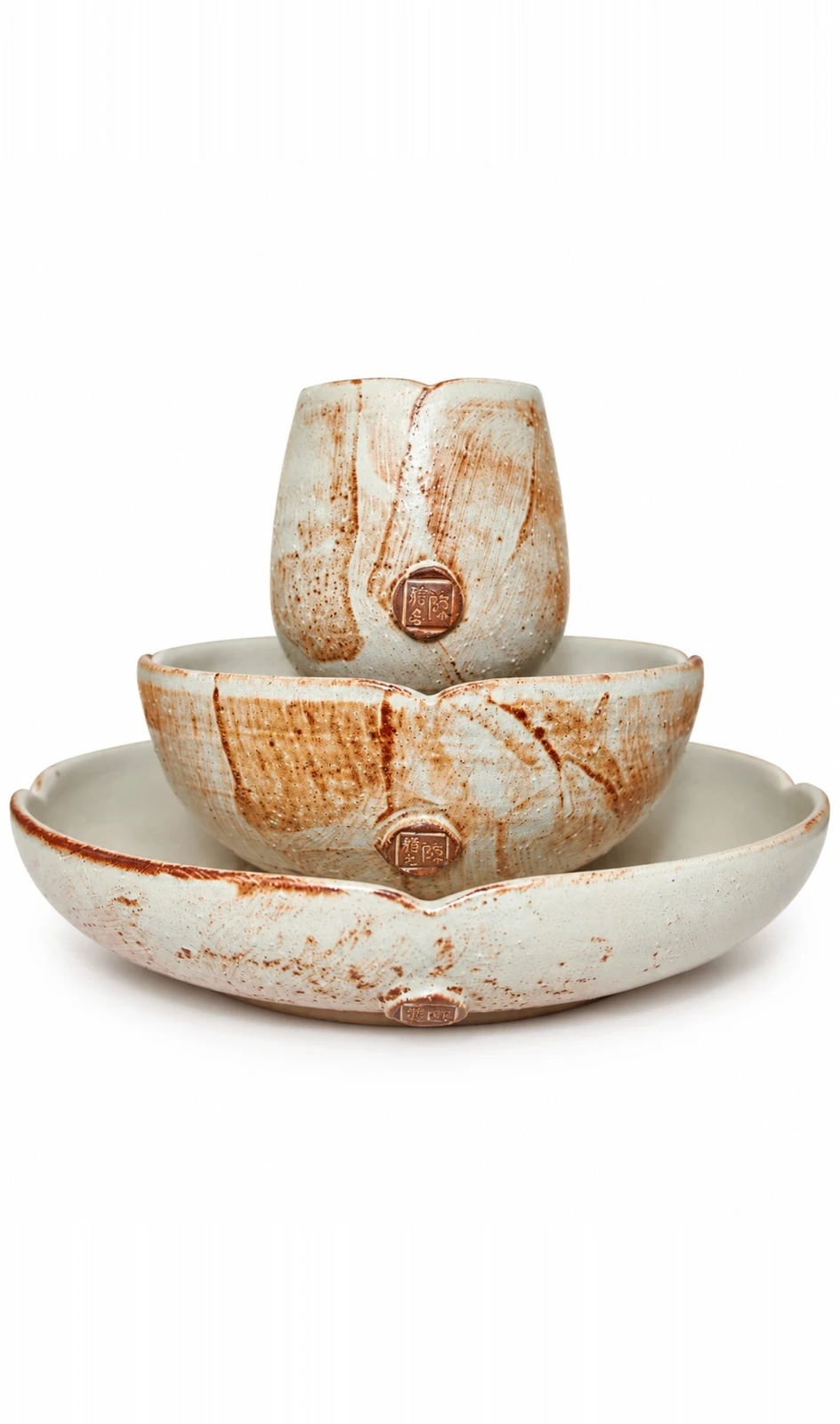 Lotus Set by Jacob Chan, a cup stacked in a bowl on a petal-rimmed plate, all in cream glaze with rust brushwork