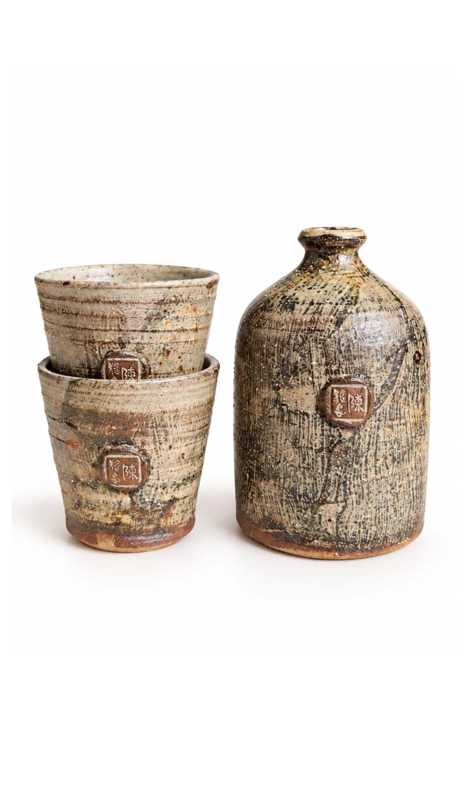 Sake Set #3 by Jacob Chan, two stacked pale speckled cups beside a textured stone-coloured bottle