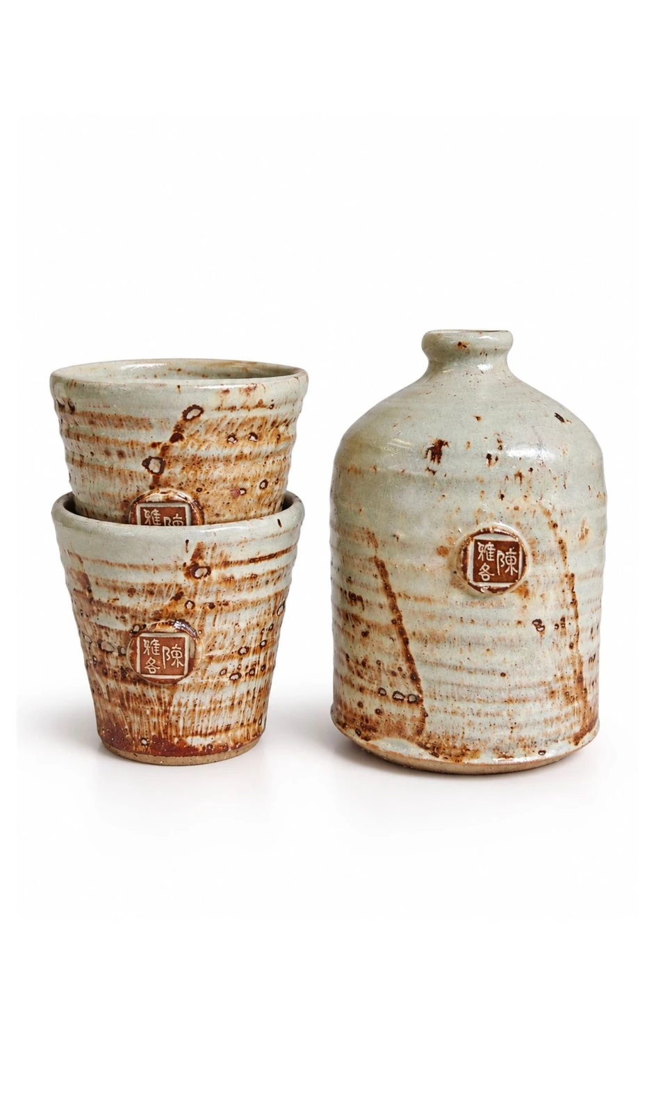 Sake Set #4 by Jacob Chan, two stacked celadon cups with rust flashes beside a pale glazed bottle