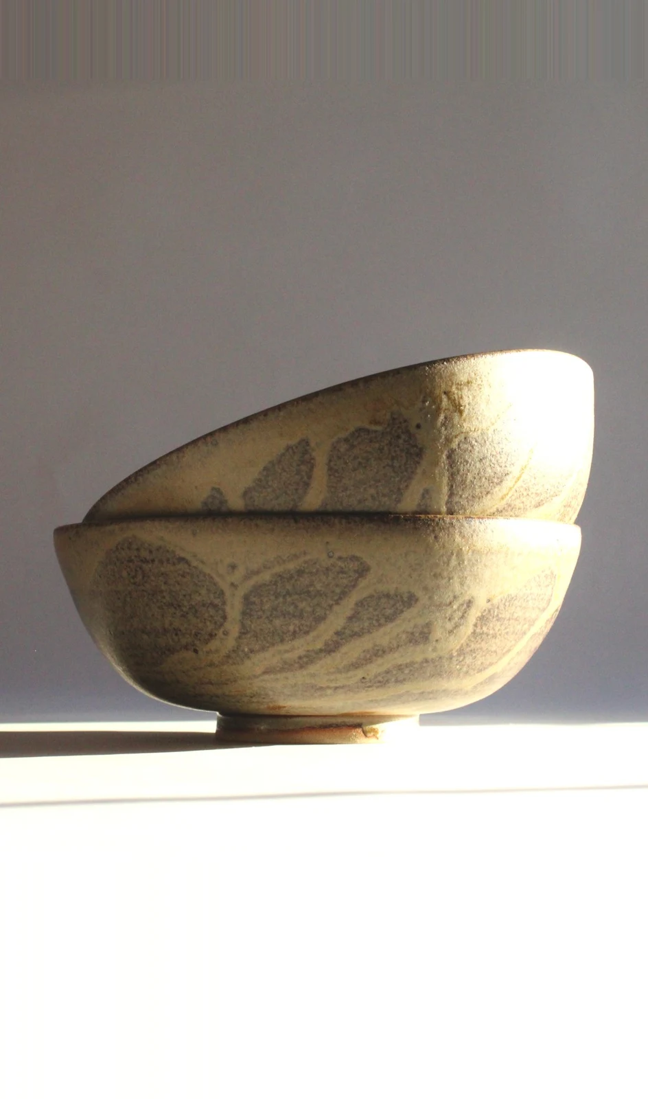 Large Bowl by James Galbraith Kirkpatrick, two stacked stoneware bowls with a speckled cream glaze and grey leaf-like marks, in low sunlight