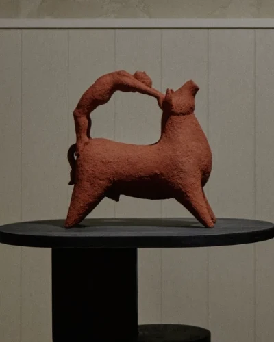 Bull Leaping II by Zahed Tajeddin, a terracotta bull with a figure arching over its back, on a black wooden plinth