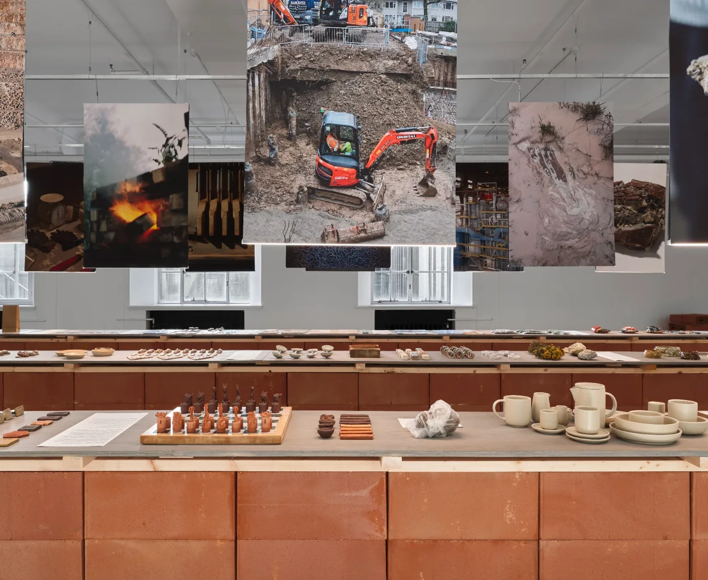 Jacob Chan's chess set, ceramics and material samples on long tables beneath hanging photographs of excavation sites