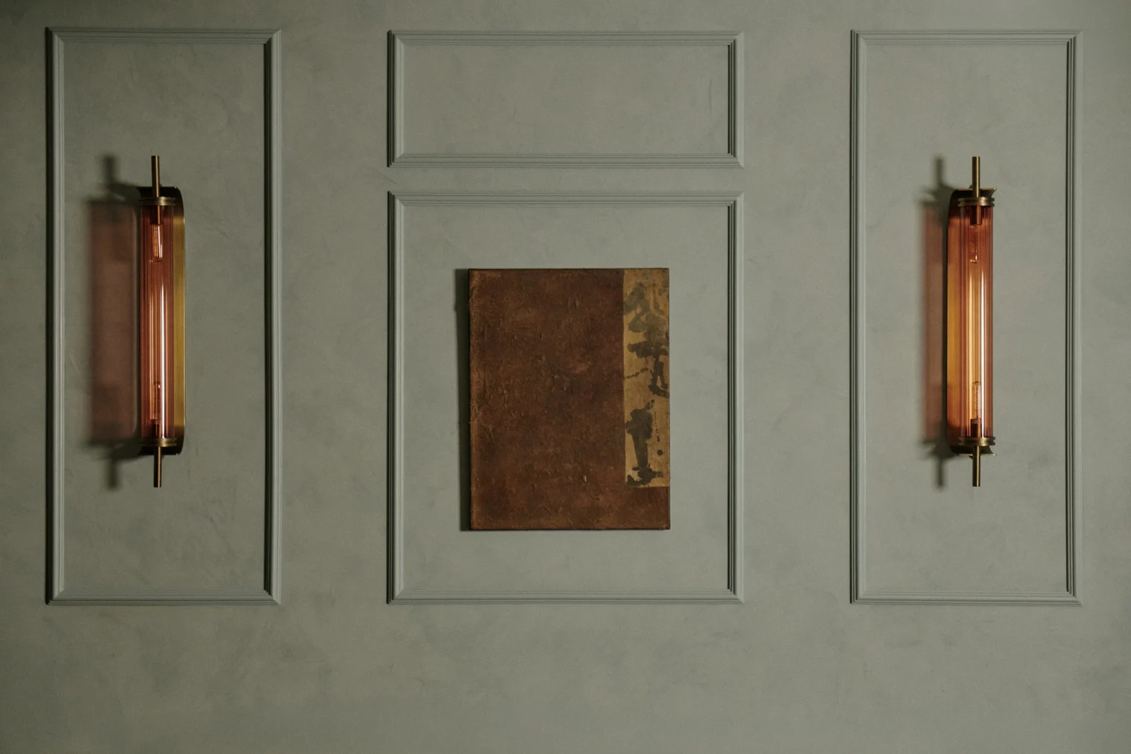 A work by Alexandra Yan Wong hung between two brass wall lights on a panelled wall